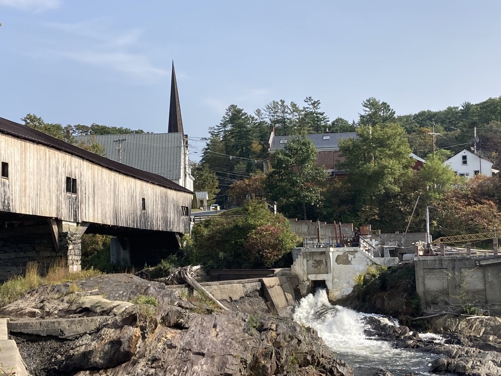 Covered bridge and church spire along a river in Bath NH
